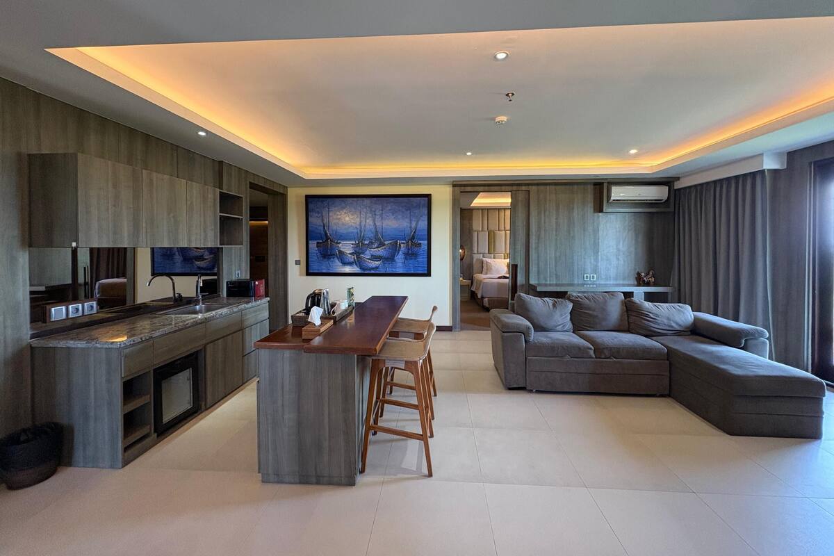 A modern living room with a sofa, a dining area with a wooden table, and a kitchen with a built-in island.