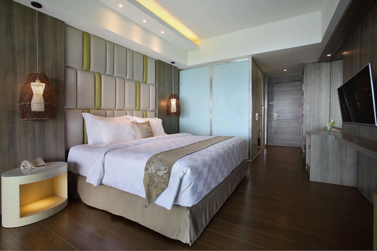 A modern hotel room with a large bed, a bedside table with a lamp, a TV, and a sliding door leading to a bathroom.