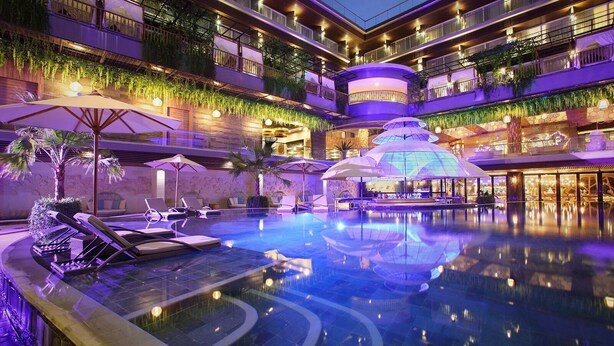 A multi-level hotel with a central swimming pool, outdoor seating, and lush greenery. - The Crystal Luxury Bay Resort Nusa Dua (Nusa Dua)
