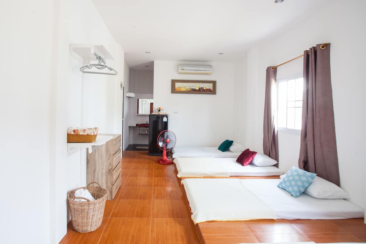 A hotel room with two beds, a fan, a refrigerator, and a window with curtains.