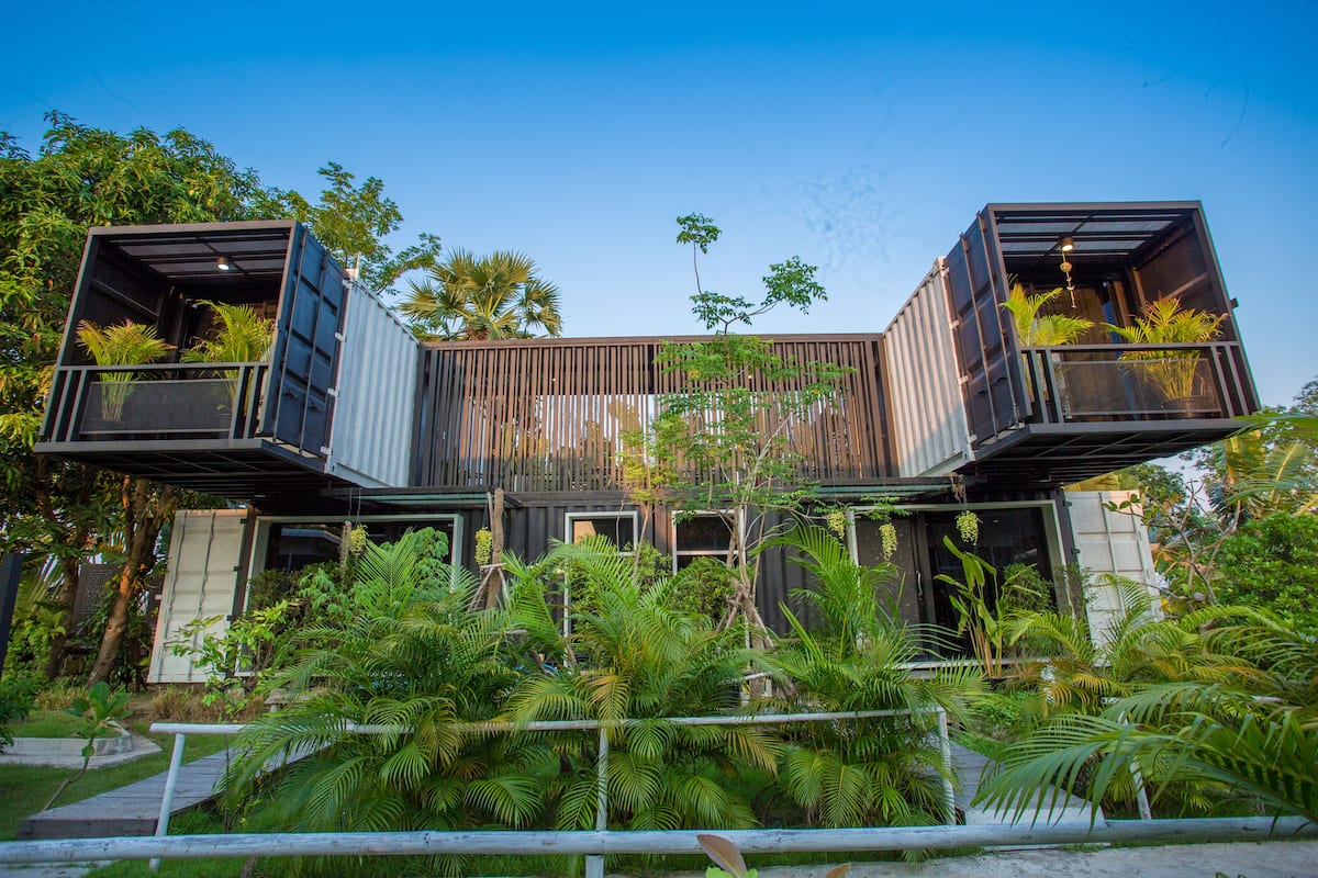A modern house with two large shipping containers as the main structure, surrounded by lush tropical vegetation.