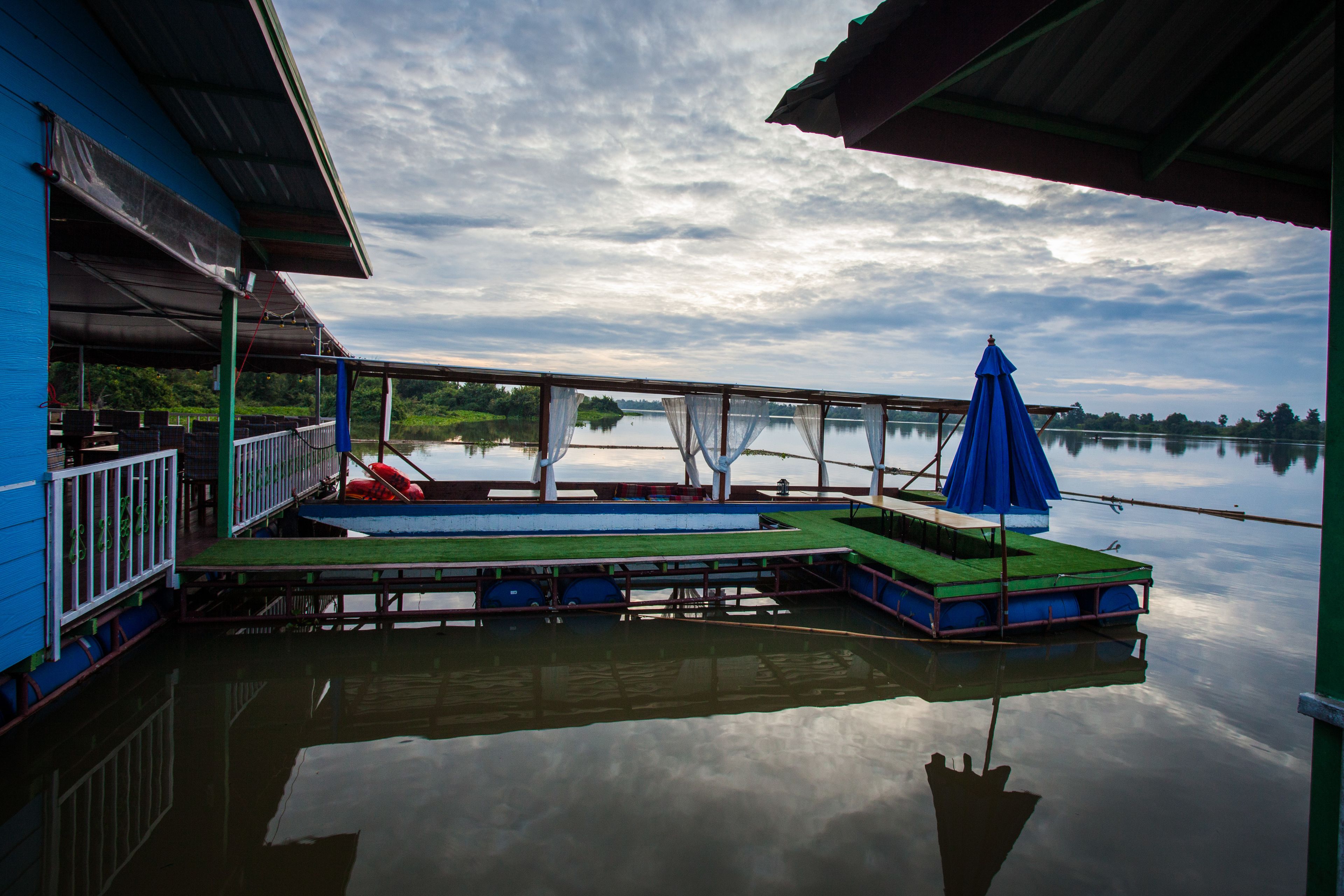 A dock with a blue building, a covered seating area, and a calm lake.