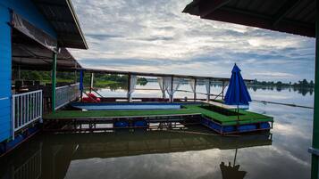 A dock with a blue building, a covered seating area, and a calm lake.