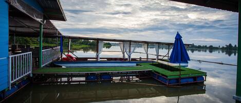A dock with a blue building, a covered seating area, and a calm lake.