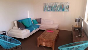 A living room with a white sofa, teal chairs, a wooden coffee table, and a modern lamp.