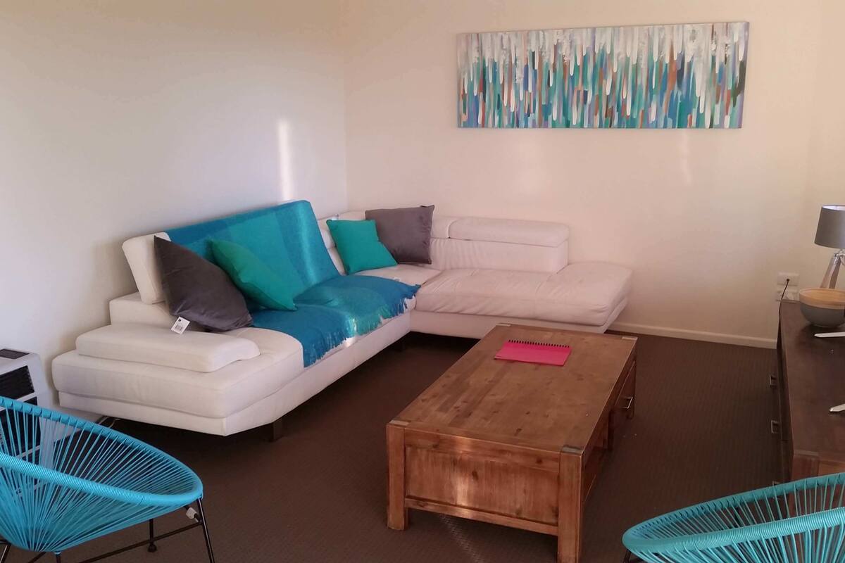 A living room with a white sofa, teal chairs, a wooden coffee table, and a modern lamp.
