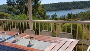 A wooden table with four chairs on a balcony overlooking a lake.