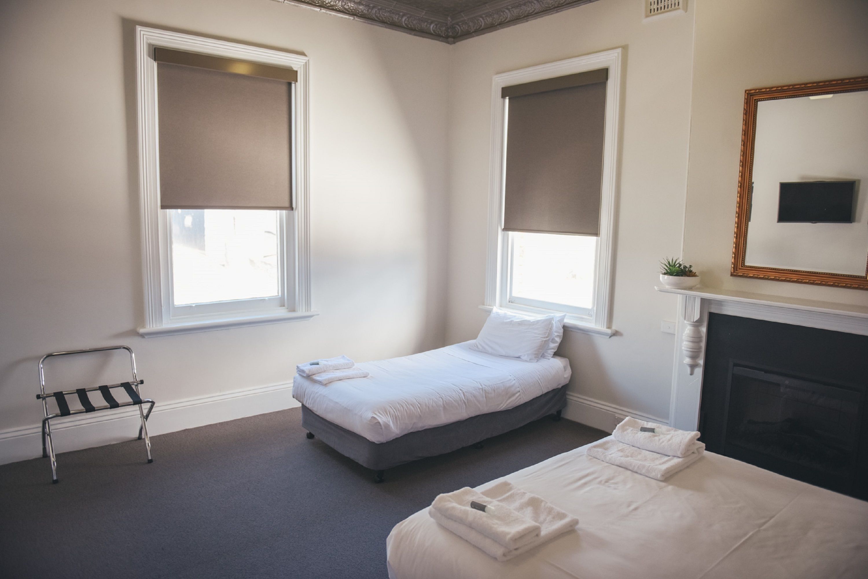 A bedroom with two beds, a small table, a chair, a fireplace, and large windows with blinds.