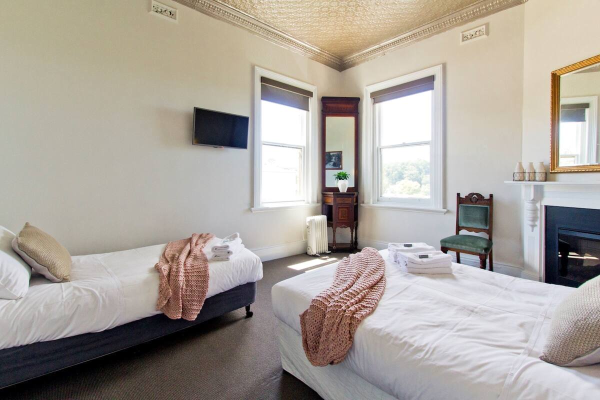 Ein Hotelzimmer mit zwei Betten, einem Fernseher, einem Kamin und großen Fenstern.
