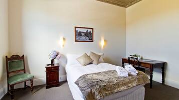 A neatly arranged hotel room with a bed, a chair, a desk, and a small table with a vase of flowers.