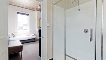 Ein modernes Hotelzimmer mit Duschabtrennung aus Glas, einem Bett mit Blick auf die Stadt und einer kleinen Sitzecke.