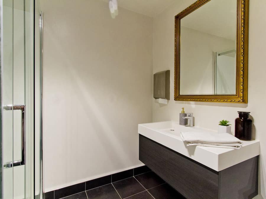 A modern bathroom with a glass shower door, a white sink with a dark vanity, and a large mirror with a gold frame.