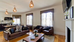 Una sala de estar moderna con un sofá, sillones, una mesa de centro y una chimenea. Se observa una cocina al fondo con una mesa de comedor y sillas.