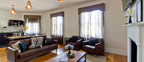 Una sala de estar moderna con un sofá, sillones, una mesa de centro y una chimenea. Se observa una cocina al fondo con una mesa de comedor y sillas.