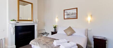 A bedroom with a bed, a fireplace, a mirror, a framed picture, and a nightstand.