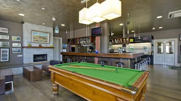 A pool table with a bar area in the background, a fireplace, and a television mounted on the wall.
