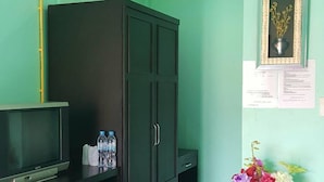 Una habitación con paredes color turquesa, un armario negro, un refrigerador pequeño, un televisor y una planta con flores.