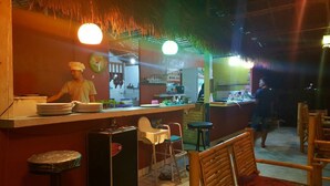 Interior de un restaurante con barra, mobiliario de madera y techo de paja.