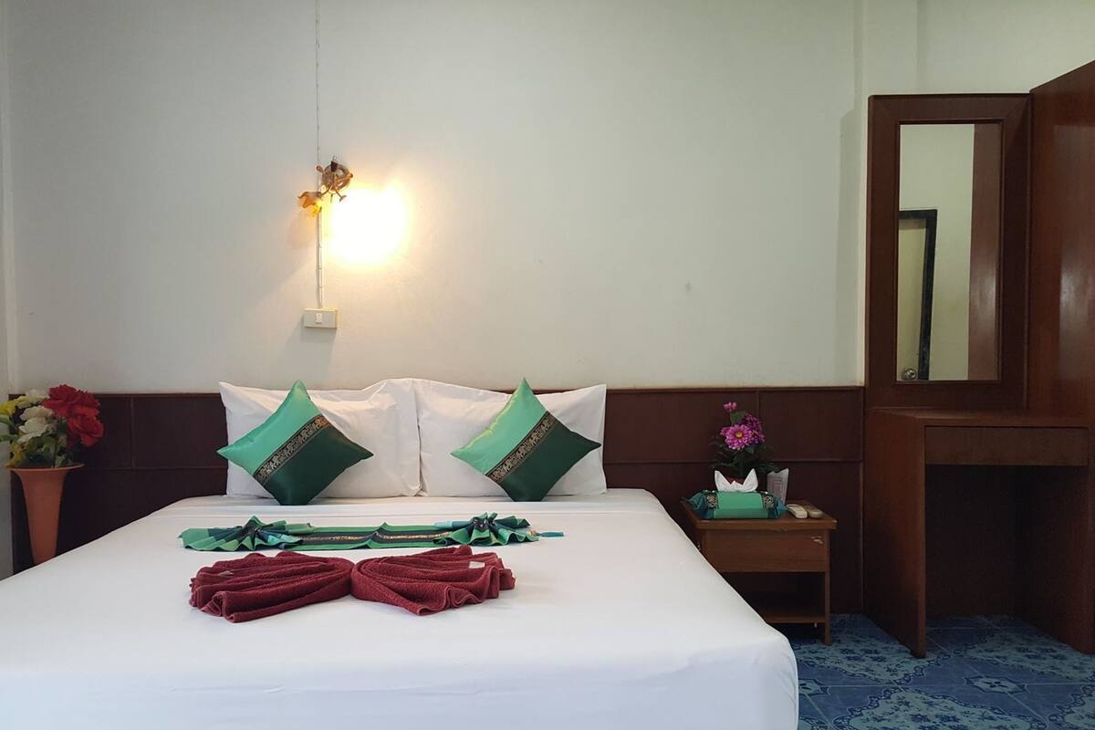 Ein Hotelzimmer mit einem ordentlich bezogenen Bett, einem Nachttisch mit Taschentuchbox, einem Spiegel und einer wandmontierten Lampe.