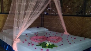 Una cama con dosel, pétalos de rosa y una almohada decorativa.