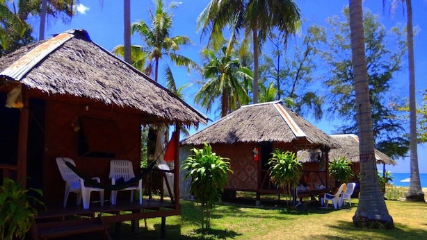 Un resort tropical con cabañas de techo de paja, sillas de plástico blancas y palmeras.