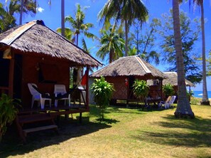 Un resort tropical con cabañas de techo de paja, sillas de plástico blancas y palmeras.