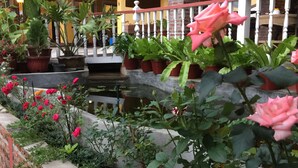 Un área ajardinada con plantas y flores en macetas, un muro de ladrillo y una barandilla blanca.