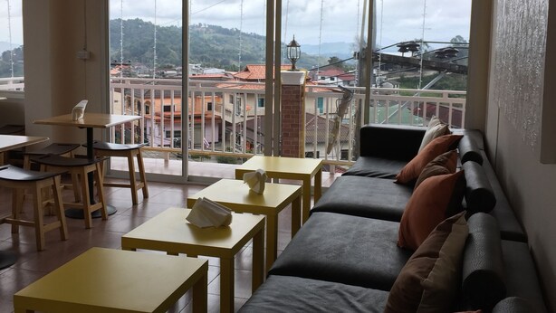 Una habitación con un ventanal grande, un sofá, mesas amarillas y un ventilador de techo.