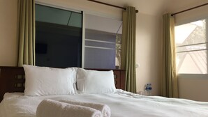 Habitación de hotel con cama, ropa de cama blanca, ventana con cortinas y vista a un edificio.