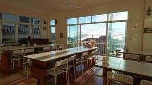 Un comedor amplio con varias mesas y sillas, ventanas grandes que ofrecen vistas del paisaje urbano, y un piano al fondo.