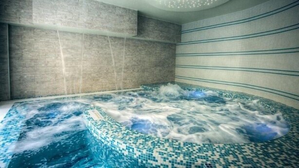 Una moderna stanza spa con una grande vasca idromassaggio, pareti piastrellate e un lampadario a soffitto.