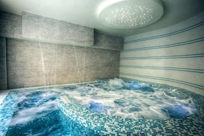 A modern spa room with a large hot tub, tiled walls, and a ceiling light fixture. - Hotel il Duca del Montefeltro (Pennabilli)