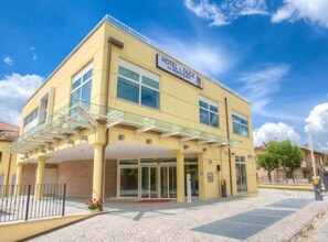 A yellow building with a sign reading "HOTEL IL DUCA." It features a glass entrance, a covered walkway, and a brick facade. - Hotel il Duca del Montefeltro (Pennabilli)