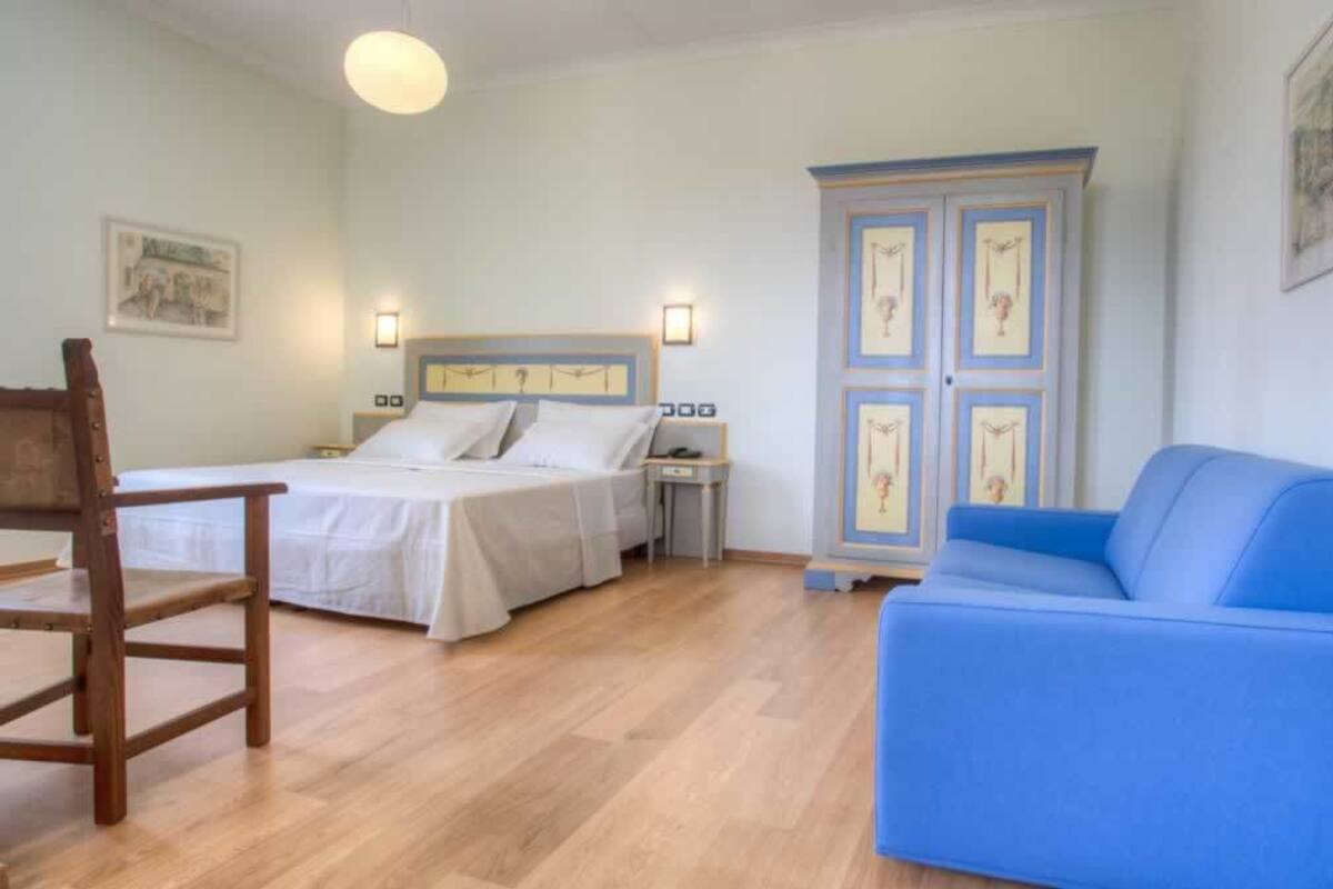 A bedroom with a bed, a blue sofa, a wooden chair, and a cabinet.