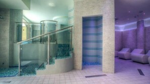 Un'area piscina moderna al coperto, con ringhiere in vetro, pavimento piastrellato e un angolo relax con poltrone imbottite.