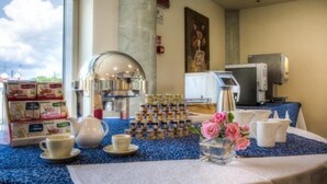 Colazione servita con macchina da caffè, teiera, tazze e un vassoio a più livelli con dolci.