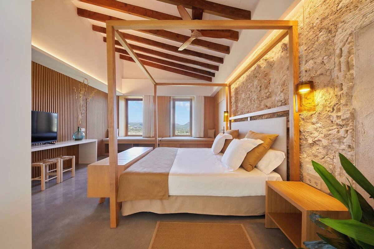 Quarto com cama de dossel de madeira, televisão e parede de pedra.