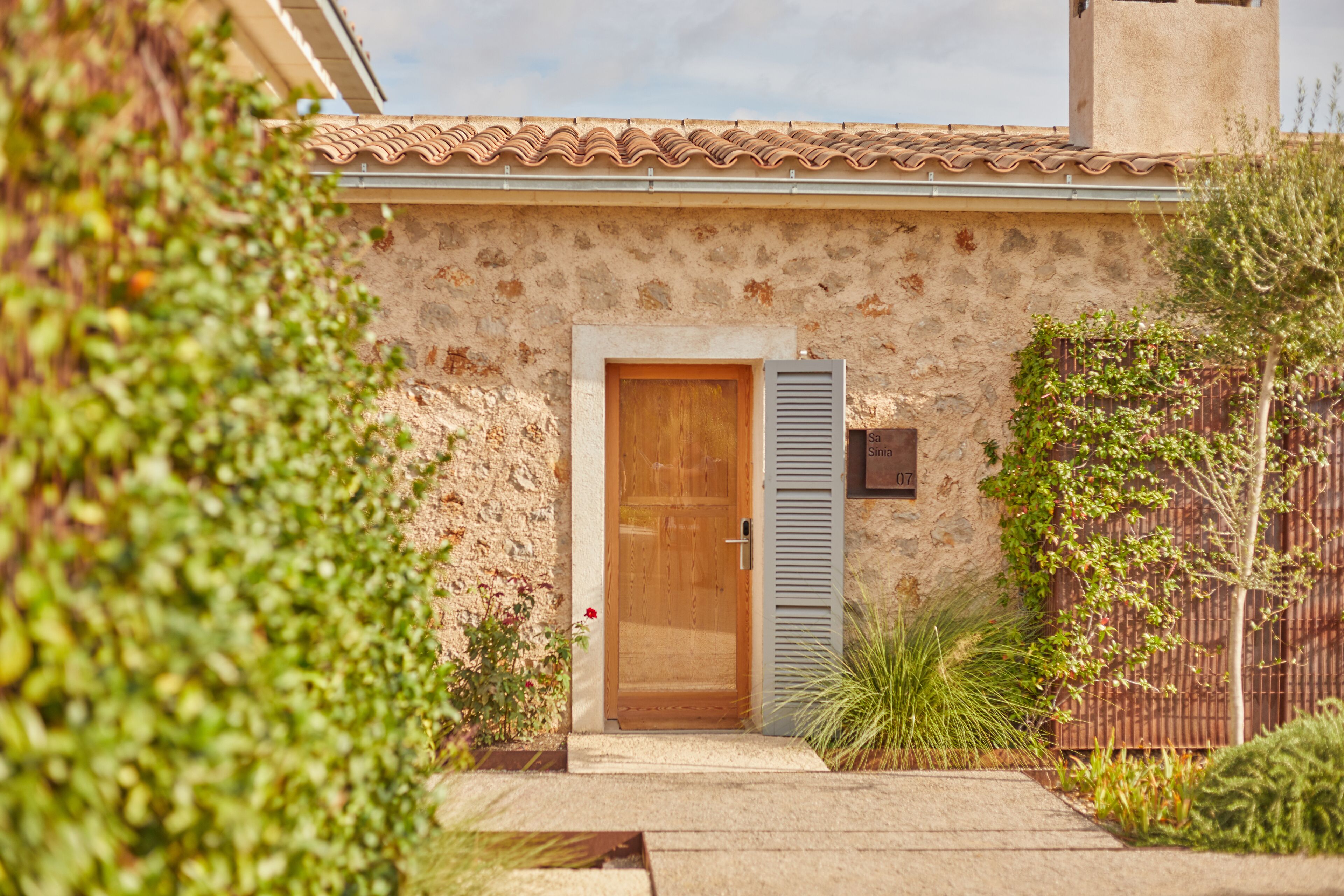 A stone building with a wooden door and a small garden area with plants and a fence.