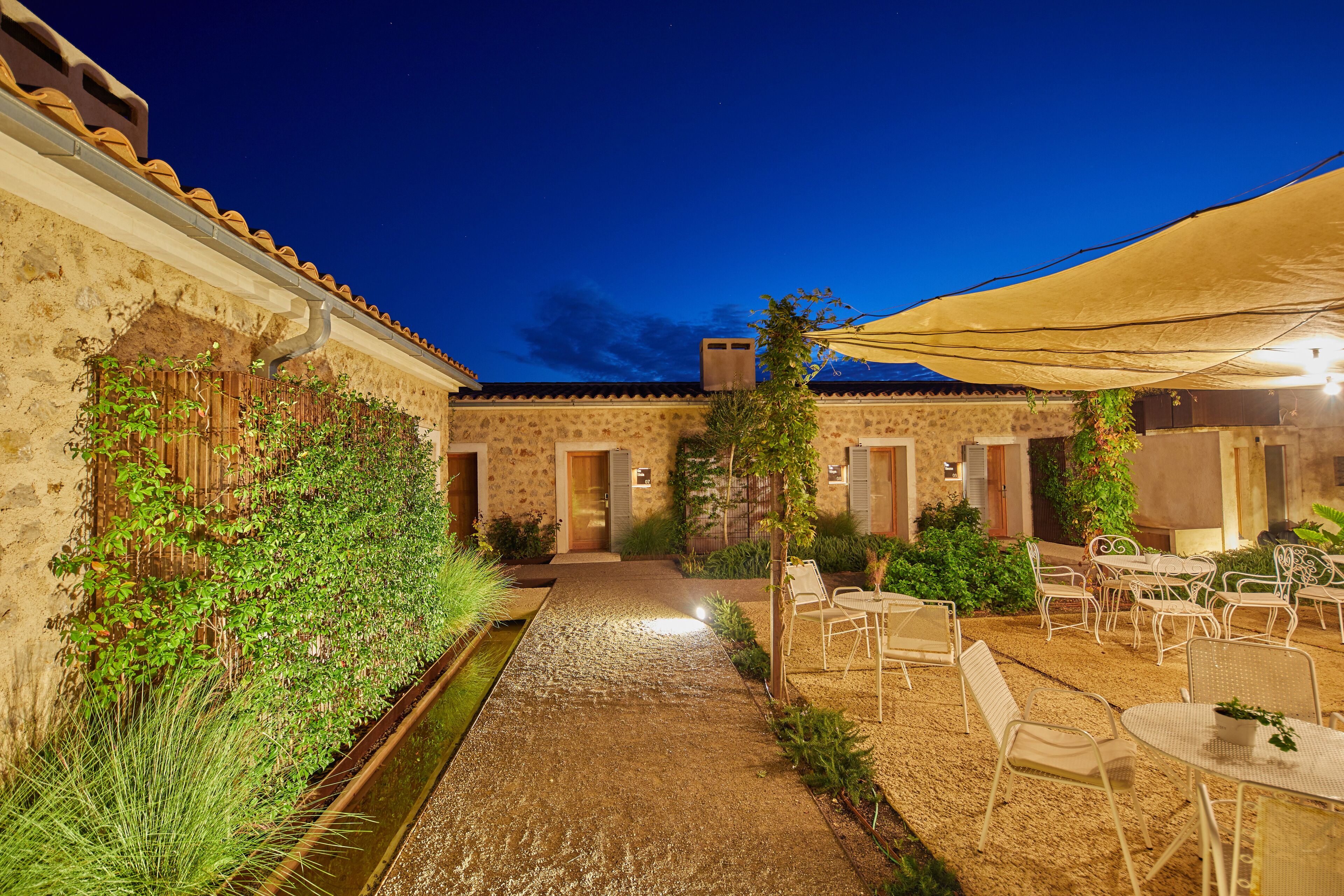 A courtyard with a paved walkway, outdoor seating area, and a building with a tiled roof.