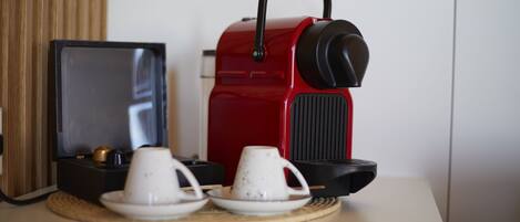 Una cafetera roja con un asa negra, una taza blanca y un plato sobre una alfombrilla tejida.
