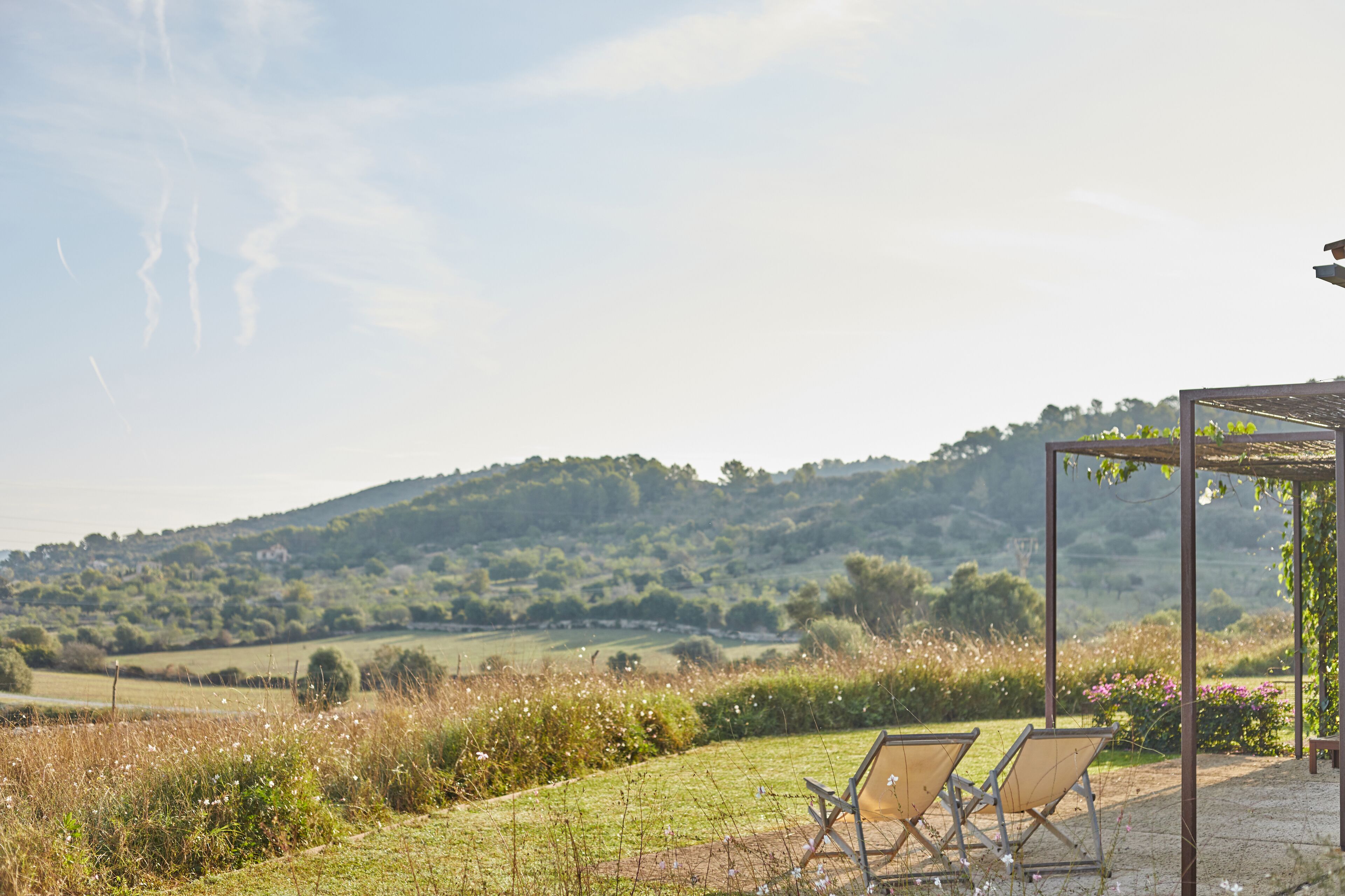 A gazebo with two chairs in a grassy area with a view of a hilly landscape.