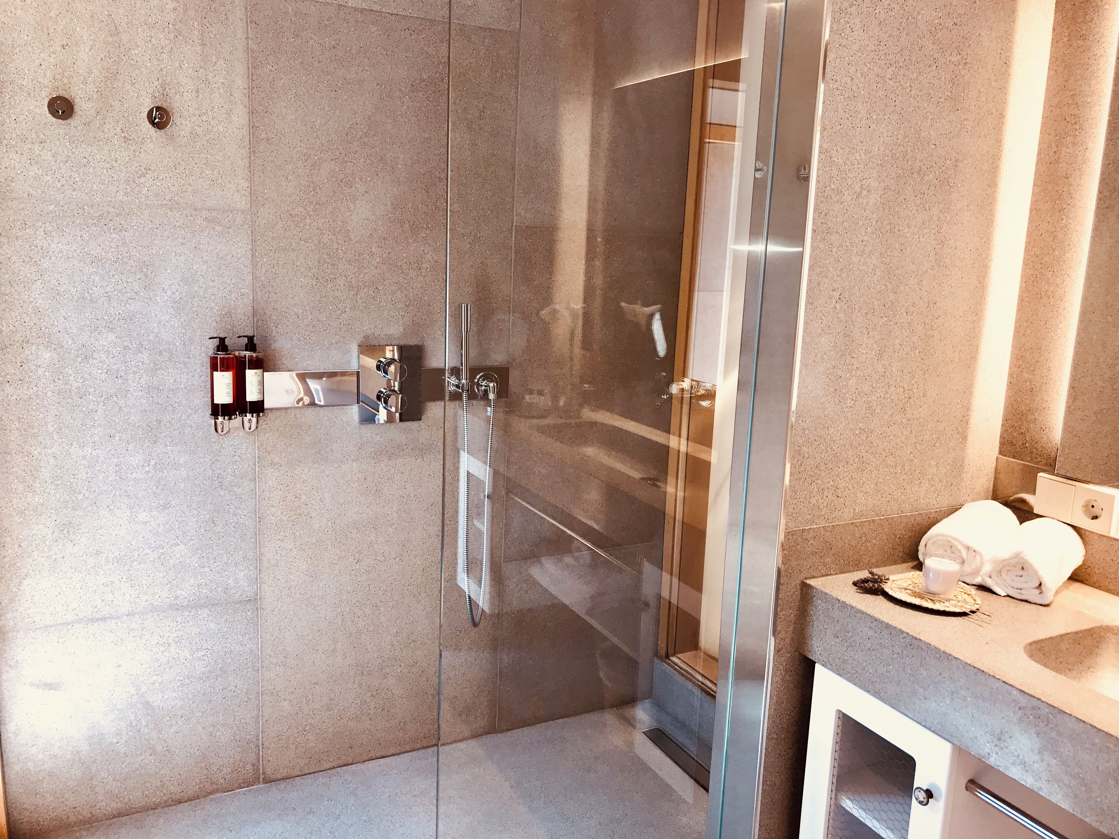 A modern bathroom with a glass-enclosed shower, a vanity with a towel and a cup, and a mirror.