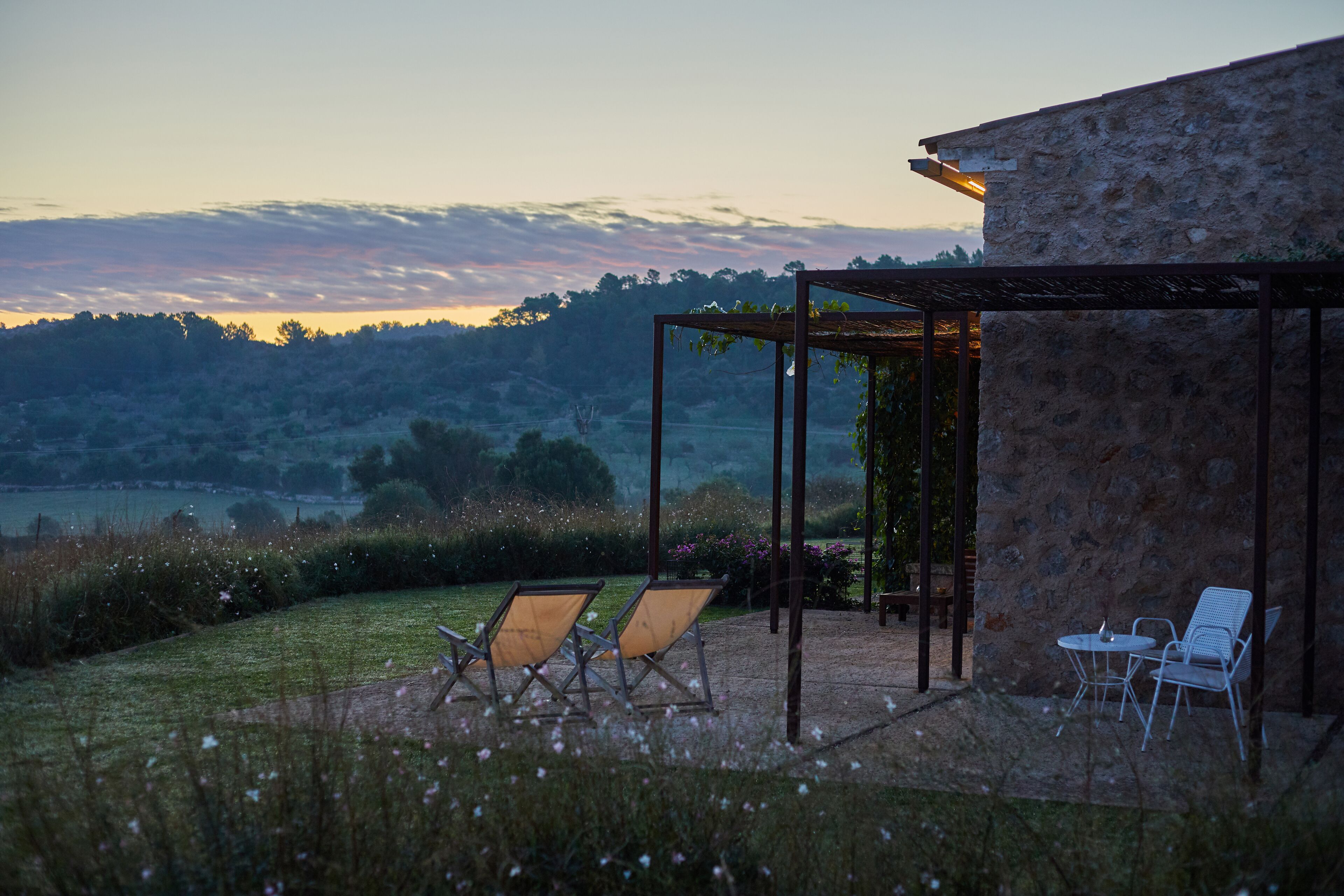 Un patio con dos sillones y una mesa, con vista a un paisaje pintoresco con colinas y cielo despejado.