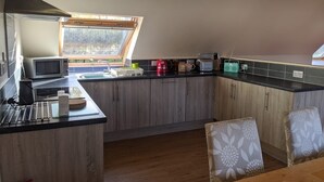 A modern kitchen with a skylight, wooden cabinets, and a dining area with patterned chairs. - Willowbarn Self-Catering Rafford (Forres)