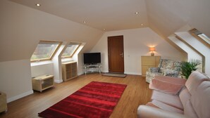 A spacious loft bedroom with a large window, a flat-screen TV, a red rug, and a cozy seating area. - Willowbarn Self-Catering Rafford (Forres)