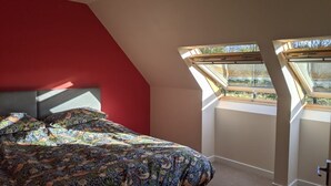 A bedroom with a sloped ceiling, a bed with a patterned bedspread, and skylights providing natural light. - Willowbarn Self-Catering Rafford (Forres)