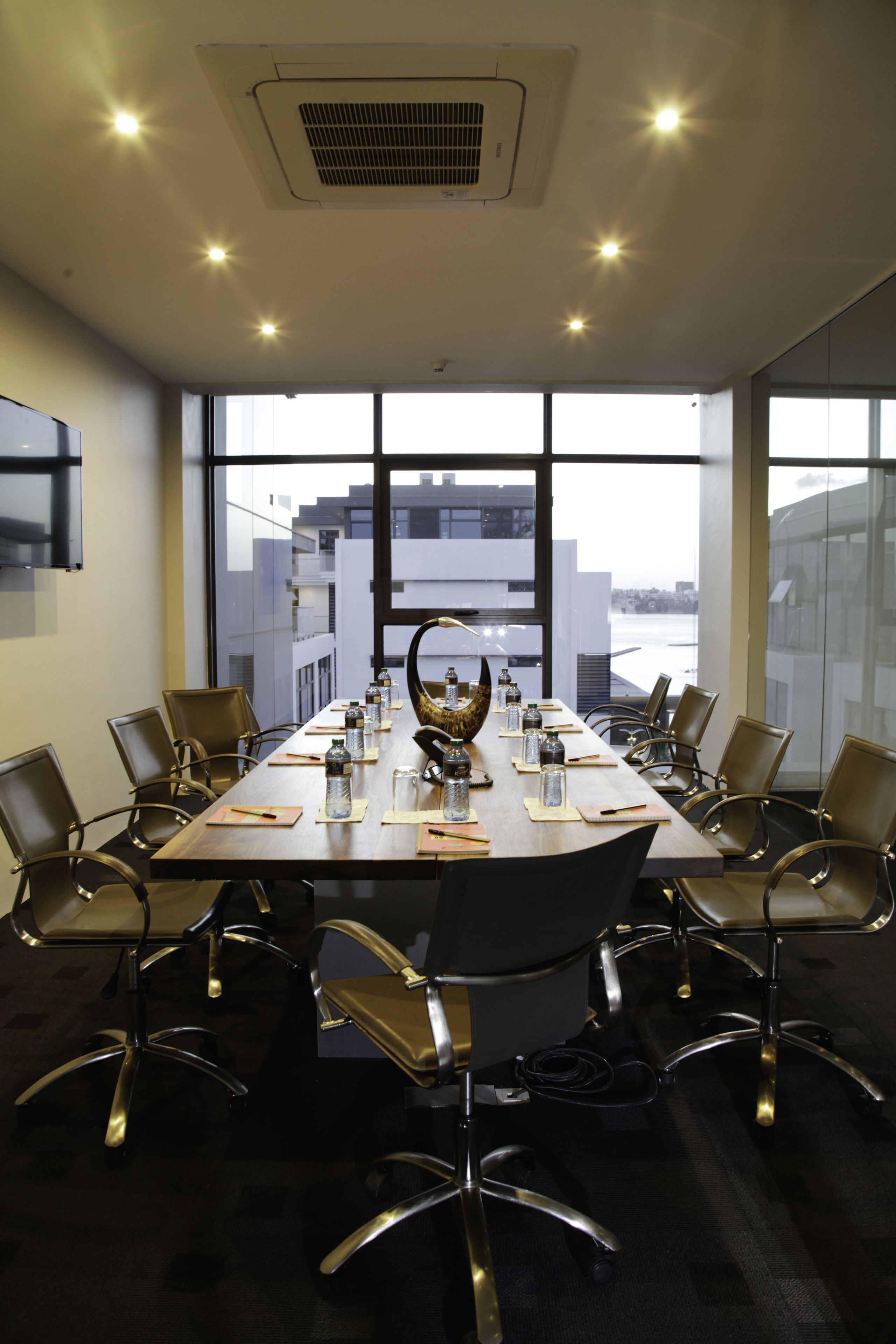 Un salón de conferencias con una larga mesa, sillas y un amplio ventanal que ofrece vistas a edificios.