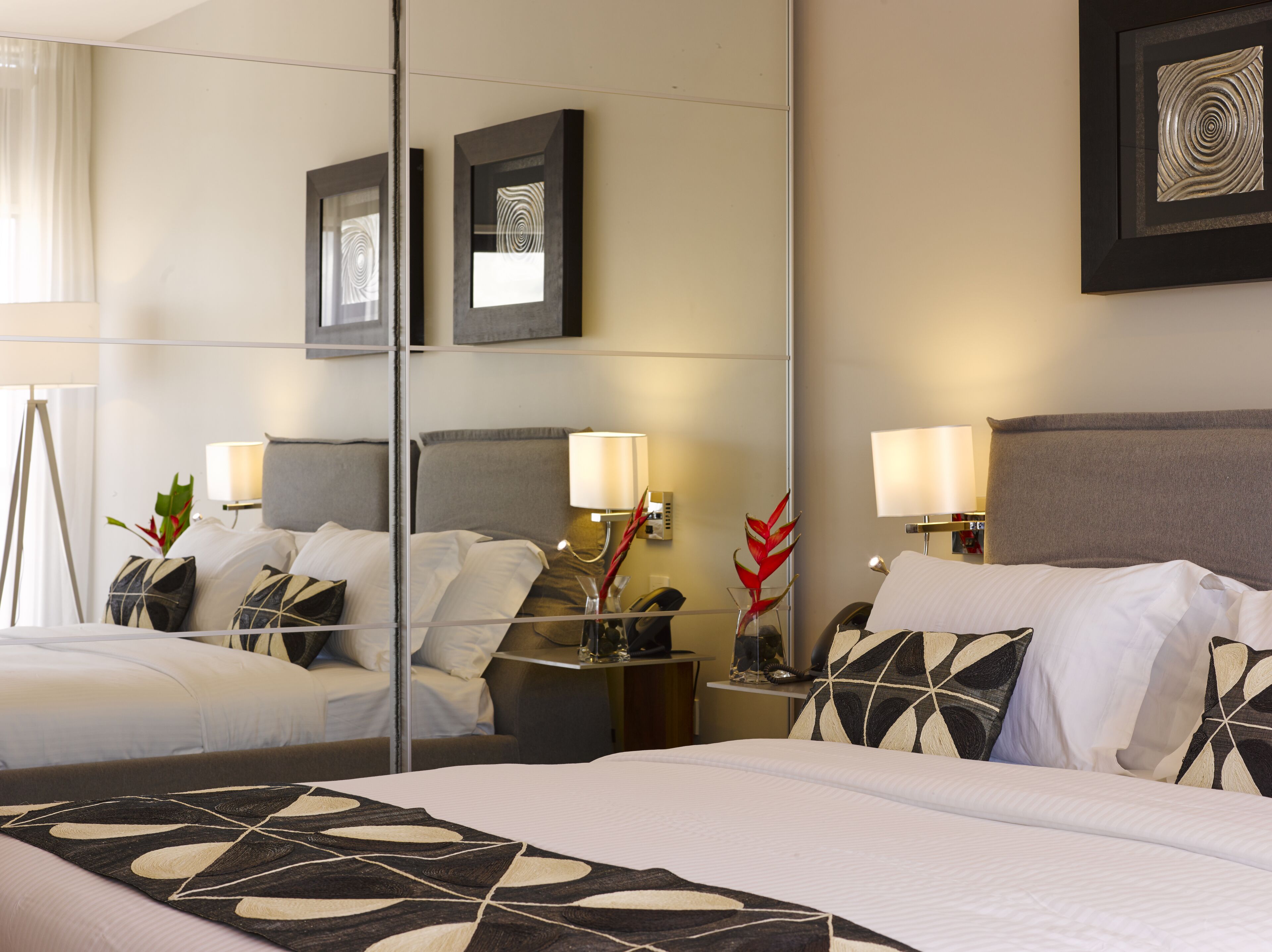 Habitación de hotel con una cama grande, mesitas de noche, lámparas y un espejo que refleja la habitación.