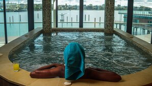 Una persona relajándose en un jacuzzi con vistas a un paisaje urbano a través de amplias ventanas.