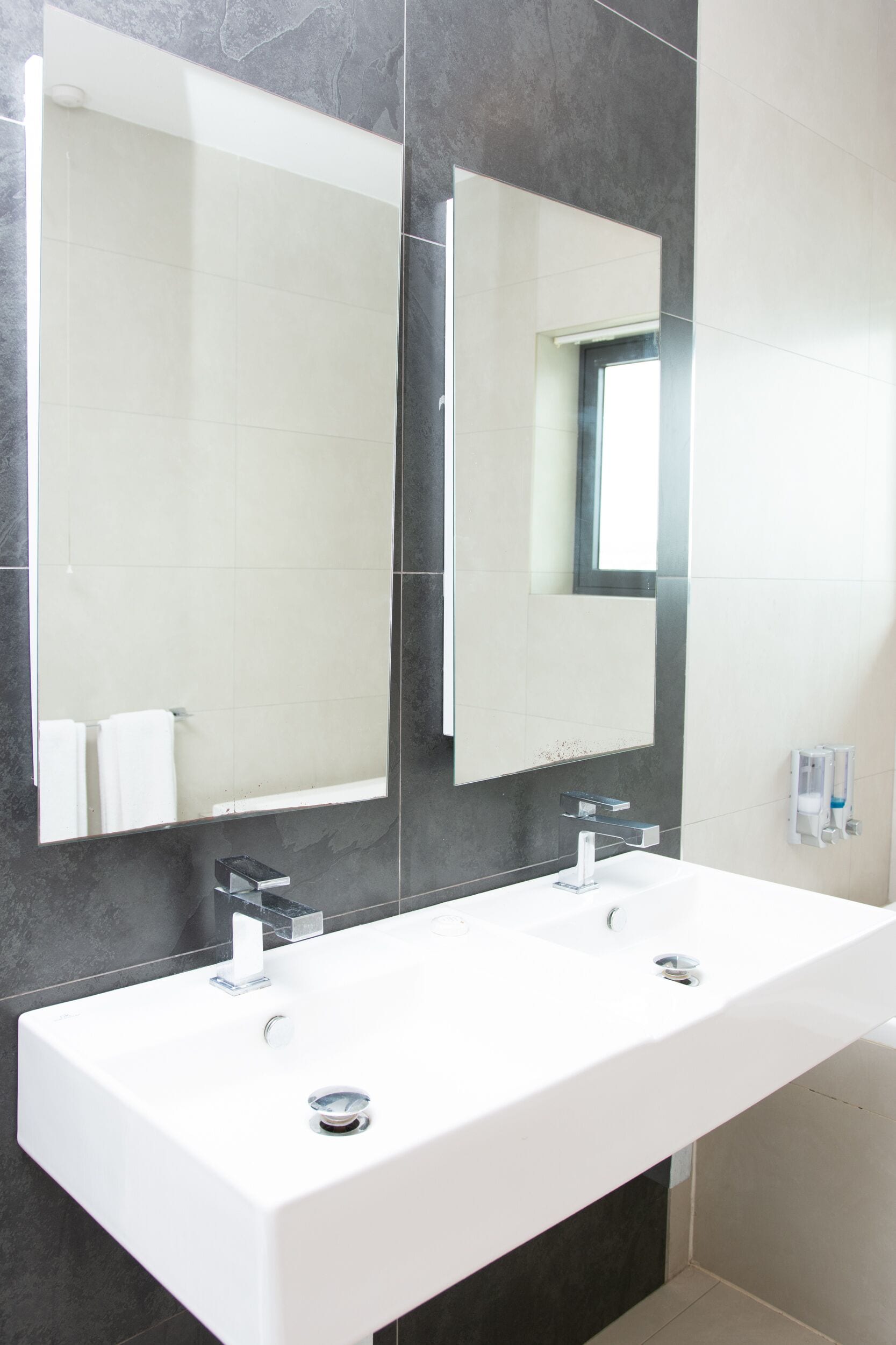A modern bathroom with a white sink, two faucets, and a large mirror.
